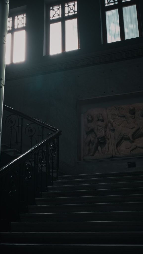 Dark museum staircase with artistic sculpture and sunlight filtering through windows.
