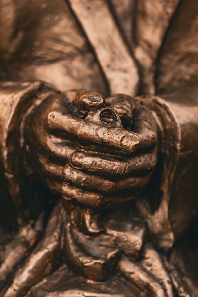 Artistic close-up of a bronze statue's hands delicately holding a ring, emphasizing texture and patina.