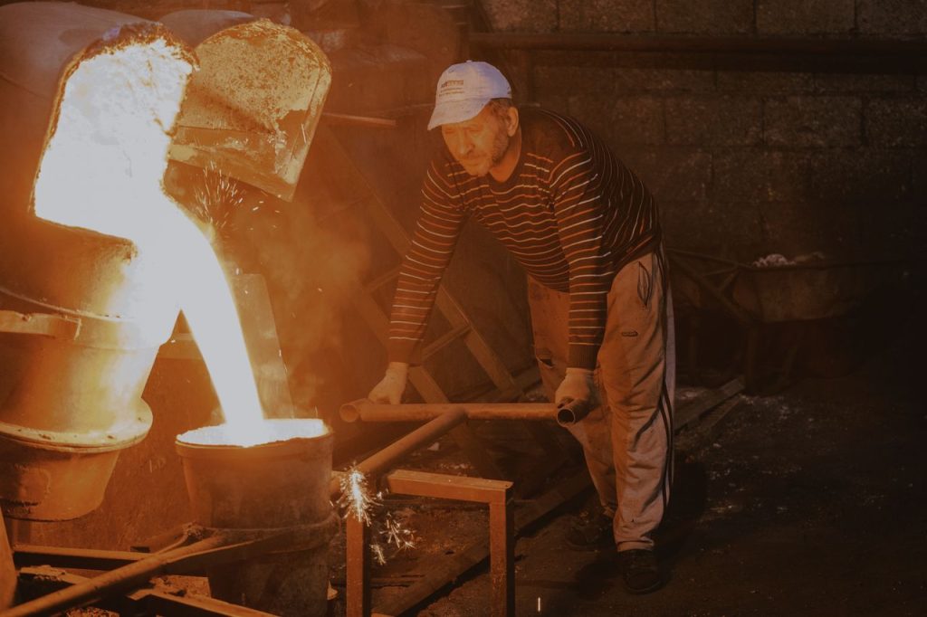 Male worker pours molten metal in a foundry setting, showcasing industrial work.