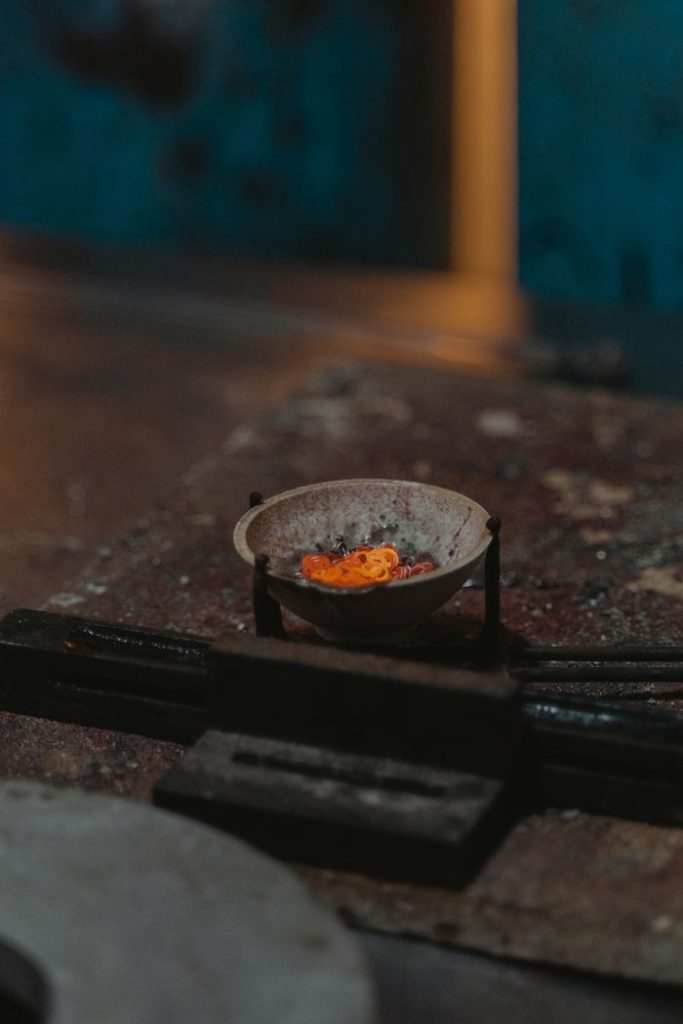 A close-up view of metal melting in a dish, set in an industrial environment with warm lighting.